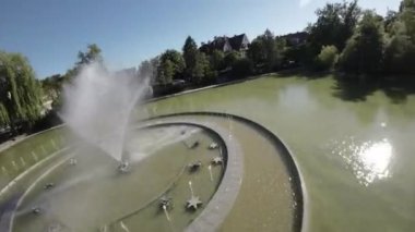 Videoda parkta bir çeşme var. Çeşme dairesel bir havuzda yer almaktadır ve havaya fışkıran uzun ve ince bir su akıntısı vardır. Havuzdaki su yeşil ve hareketsiz. Var.