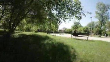 Video, güneşli bir günde parkta yürüyen bir insanın birinci şahıs perspektifi. Park yemyeşil ağaçlar, yeşil çimenler ve çeşitli bitkilerle doludur. Ayrıca birkaç bank ve birkaç tane de bank var.
