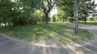 Güneşli bir günde koruyucu giysili bir patenci parkın içinden geçer. Park yemyeşil ağaçlar, yeşil çimenler ve renkli çiçeklerle dolu. Paten bir bankın, bir ağacın ve küçük bir bankın yanından geçiyor.