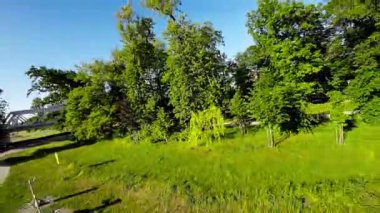 Güzel bir parkta rahatça dolaşın ve doğa manzarası ve seslerinin tadını çıkarın. Bereketli ağaçlar, renkli çiçekler ve sakin bir nehir rahatlatıcı ve huzurlu bir atmosfer yaratır.