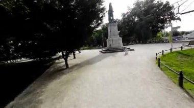 Video, Polonya 'nın Opole kentinde Silezya Ayaklanması anıtı olan bir parkı gösteriyor. Park çeşitli ağaçlar, çalılar ve çiçeklerle yemyeşil ile dolu. Çalışan asfalt bir yol var.