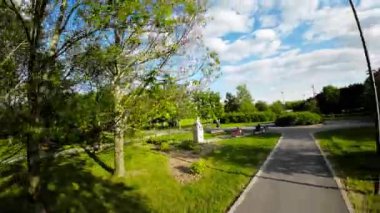 Polonya, Opole 'da güzel bir park, yemyeşil ağaçlar, asfalt bir yol ve bir bank. Güneş ağaçların arasından parlıyor, yerde noktalı bir desen oluşturuyor. Rahatlamak ve eğlenmek için mükemmel bir yer.