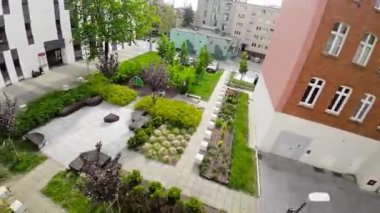 Bu 4K hava görüntüleri yeşil bahçeli modern bir apartman binasını gösteriyor. Video kuş bakışı görüntüden çekiliyor ve binaları ayrıntılı olarak gösteriyor. Binalar ağaçlarla çevrili.