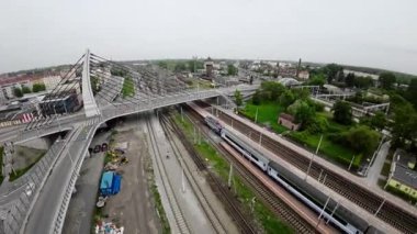 Video, Polonya 'nın Opole kentinde bir tren istasyonu, bir otobüs durağı ve Oder Nehri üzerindeki bir köprüyü gösteriyor. Tren istasyonu şehir merkezinde yer almaktadır ve şehir için büyük bir ulaşım merkezidir. Şey...