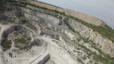 Video, kayalık bir taş ocağının kapsamlı bir hava görüntüsünü sunuyor. Taş ocağı engebeli uçurumları, düzensiz arazisi ve seyrek bitki örtüsüyle karakterize edilir. Taş ocağının duvarları...