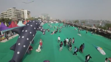 Video, Ahmedabad Uluslararası Uçurtma Festivali 'ni gösteriyor. Festival, arka planda bir nehir bulunan büyük yeşil bir alanda gerçekleşiyor. Çeşitli renklerde uçurtma uçuran bir sürü insan var.