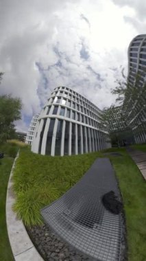 Bu cam cepheli ve ahşap geçitli modern bir ofis binasının sanal bir turu. Bina ağaçlarla çevrili ve yeşil bir çimenliği var. Video, bir kişinin bakış açısından çekilmiştir.