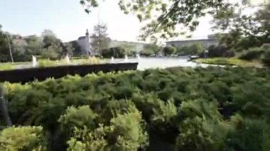 Güneşli bir günde parkta huzurlu bir yürüyüş bu. Park ağaçlar, çalılar ve çiçekler de dahil olmak üzere yemyeşil ile doludur. Ayrıca birkaç bank ve bir çeşme de var. Park harika bir yer.