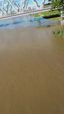 Video, nehrin üzerindeki bir köprünün hava görüntüsüyle başlıyor. Nehir şiş ve çamurlu, ve kıyıları taşmış, çevreyi su basmış. Su, suyun dibine ulaştı.