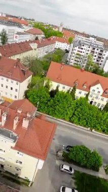 Video yukarıdan bir şehrin caddesini gösteriyor. Sokak ağaçlar ve binalarla dolu. Sokakta park etmiş arabalar ve kaldırımda yürüyen insanlar var. Video bir İHA 'dan alındı.