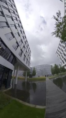 Video, birkaç binası olan modern bir ofis parkını gösteriyor. Binalar cam ve betondan yapılmıştır ve modern bir tasarıma sahiptir. Binaların önünde bir gölet var ve bir patika yan yana uzanıyor.