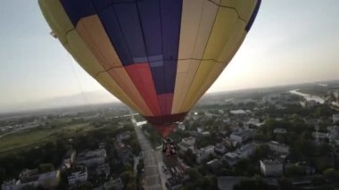 Nefes kesen hava görüntülerinde sakin bir sıcak hava balonu manzaralı bir şehir ve nehir üzerinde geziniyor. Balonların canlı renkleri aşağıdaki sakin şehir manzarasıyla tezat oluşturarak görsel olarak