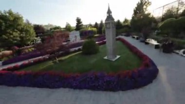 Bu, güzel bir bahçede yürüyüşün videosu. Bahçede birçok farklı çiçekler, bitkiler ve ağaçlar var. Küçük bir şelalesi ve çeşitli bahçe süslemeleri olan bir gölet var.