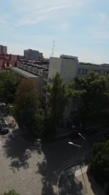 Video, her iki tarafında ağaçlar olan bir caddenin görüntüsüyle başlıyor. Kamera sağa dönüyor, binaları sırayla gösteriyor. Binalar konut ve ticari mülklerin karışımı. Şey...