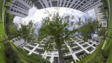 Bu, modern bir apartmanın avlusunda çekilmiş balık gözü merceği videosu. Video yerden çekiliyor ve gökyüzüne bakıyor, mavi renkli, kabarık beyaz bulutlarla. Avlu...