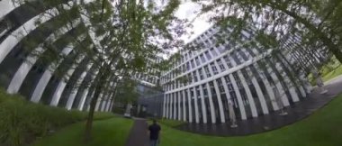 Video, cam cepheli ve yeşil avlusu olan modern bir ofis binasını gösteriyor. Bina modern bir tasarıma sahiptir ve ağaçlar ve bitkilerle çevrilidir. Avlu çok popüler bir yerdir.