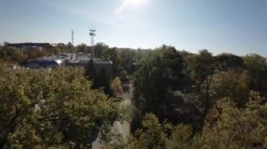 Sonbaharda parkın üzerinde birinci şahıs FPV uçuşu. Ağaçlar tamamen yeşildir ve yapraklar kırmızı, turuncu, sarı ve yeşildir. Güneş parlıyor ve orada...