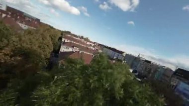 Video, apartman binaları ve evleri olan bir yerleşim bölgesinin kuş bakışı görüntüsüyle açılıyor. Kamera, her iki tarafında da arabaların olduğu bir caddeyi gösteriyor. Kamera çalışmaya devam ediyor.