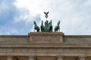 Almanya, Berlin 'deki Brandenburg Kapısı' nın tepesine yakın çekim. Çerçevenin ortasında, dört atlı bir at arabası süren tanrıça Victoria 'nın resmedildiği 