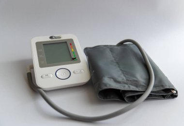 Beyaz bir yüzeye düzgünce yerleştirilmiş tıbbi malzemelerin bileşimi. Çerçevenin ortasında kan basıncını ölçmek için manşetli dijital bir tonometre var. Yanında şeffaf bir çantada elektronik bir termometre var..