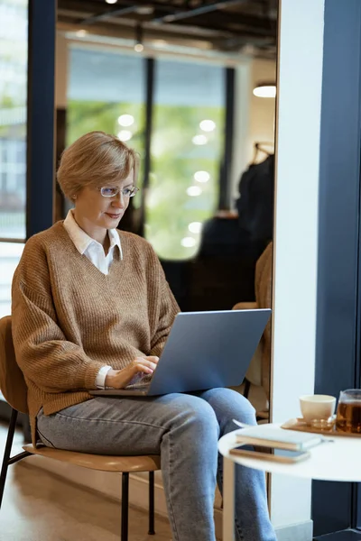 カフェでノートパソコンを操作するカジュアルな服を着た中年ビジネス女性 フリーランスの仕事のコンセプト — ストック写真