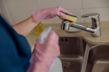 Kadın koruyucu eldivenler içinde sünger ve spreyle musluğu temizliyor. Genel temizlik kavramı