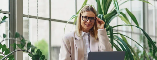 現代のオフィスに座っている間 ラップトップで働く大人のビジネス女性を笑顔 ぼやけた背景 — ストック写真