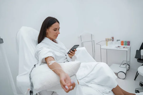 Vrouw Witte Badjas Gebruik Telefoon Tijdens Medische Procedure Schoonheidskliniek Hoge — Stockfoto