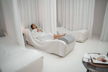 Beyaz bornozlu mutlu kadın spa salonunda bir fincan kahveyle eğleniyor.