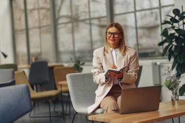 Gözlüklü kadın muhasebeci iş sırasında rahat ofisteki dizüstü bilgisayarda not alıyor. Yüksek kalite fotoğraf