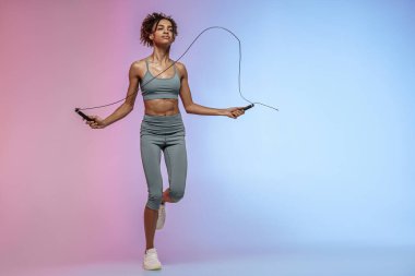 Stüdyo arka planında renk filtresiyle ip atlayan bir kadın. En iyi kardiyo çalışması
