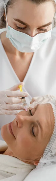 クリニックで成熟した女性クライアントへの注射を作る女性美容師の垂直ショット クローズアップ — ストック写真