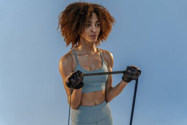 Spor giyim sektöründe güçlü bir kadın stüdyo arka planında direnç bandıyla fitness egzersizleri yapıyor.