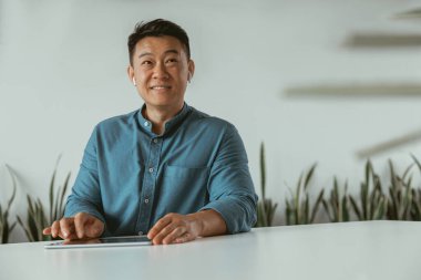 Gülümseyen Asyalı işadamı rahat ofisinde otururken dijital tablet üzerinde çalışıyor. İş konsepti