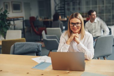 Woman working on laptop in modern coworking while sitting near colleagues. High quality photo clipart