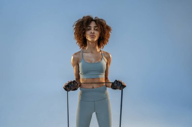 Spor giyim sektöründe güçlü bir kadın stüdyo arka planında direnç bandıyla fitness egzersizleri yapıyor.