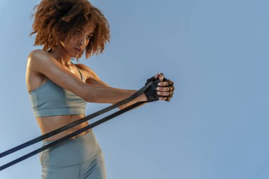 Spor giyim sektöründe güçlü bir kadın stüdyo arka planında direnç bandıyla fitness egzersizleri yapıyor.