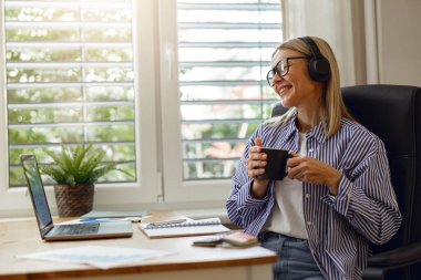 Mola sırasında evden çalışırken kahve içen gülümseyen kadın. Mesafe çalışma kavramı