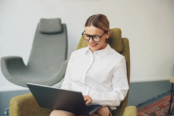ビジネスマンの女性が椅子に座って 同僚の背景にラップトップで作業しています 高品質の写真 — ストック写真