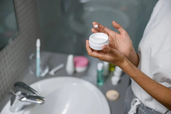 Woman applying anti-wrinkle cream standing behind mirror in home bathroom.High quality photo