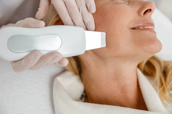 Profesjonalny Kosmetolog Robi Ultradźwiękowe Czyszczenie Twarzy Dla Pięknej Dojrzałej Blondynki — Zdjęcie stockowe