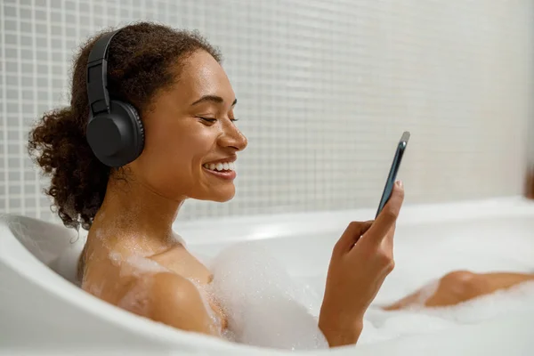 Mujer Afroamericana Auriculares Está Utilizando Teléfono Inteligente Tomar Baño Foto — Foto de Stock