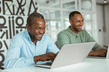 Dizüstü bilgisayarda çalışan Afrikalı iş adamı iş arkadaşlarının arka planında oturuyor. Yüksek kalite fotoğraf