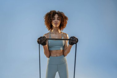 Spor giyim sektöründe güçlü bir kadın stüdyo arka planında direnç bandıyla fitness egzersizleri yapıyor.