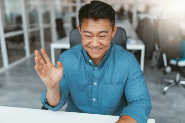 Gülümseyen Asyalı işadamı ofiste müşteriyle internette konuşuyor. Bulanık arkaplan
