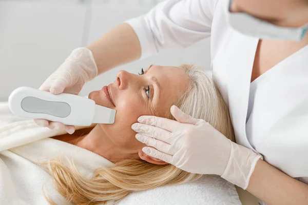 Profesjonalny Kosmetolog Robi Ultradźwiękowe Czyszczenie Twarzy Dla Pięknej Szczęśliwej Białej — Zdjęcie stockowe