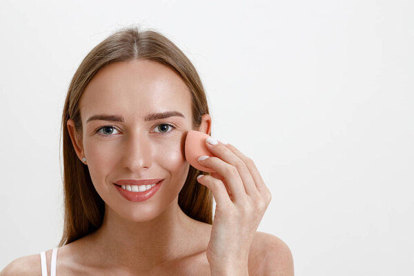 Молодая женщина держит розовую губку для нанесения косметических средств красоты на лицо. Высокое качество фото