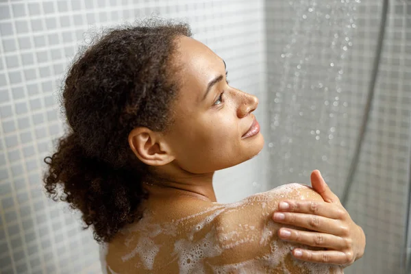 stock image Close up of african woman taking a shower with gel or shampoo foam in bathroom. High quality photo