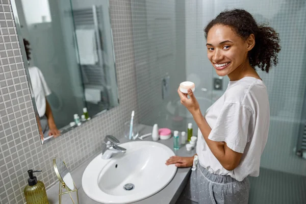 Smiling woman applying anti-wrinkle cream standing behind mirror in home bathroom.High quality photo