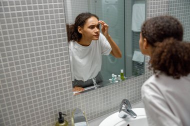 Banyoda aynaya bakarken yüzünde sivilce bulan bir kadın. Yüksek kalite fotoğraf